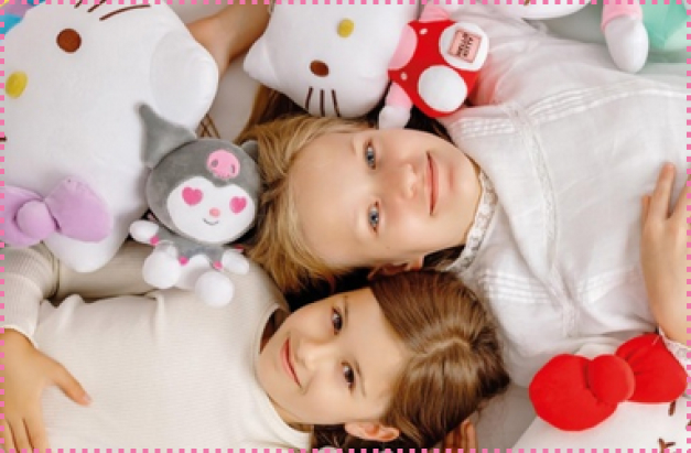 Dwie dziewczynki leżą obok siebie na łóżku, otoczone pluszowymi maskotkami Hello Kitty i Kuromi. Uśmiechają się, przytulając miękkie zabawki w pastelowych kolorach.