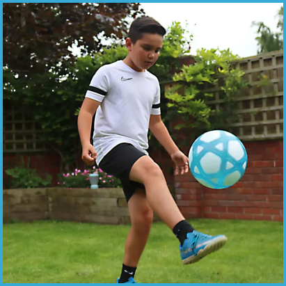 Chłopiec w sportowym stroju trenuje podbijanie interaktywnej piłki Counter Ball Smart Ball na trawniku w ogrodzie.