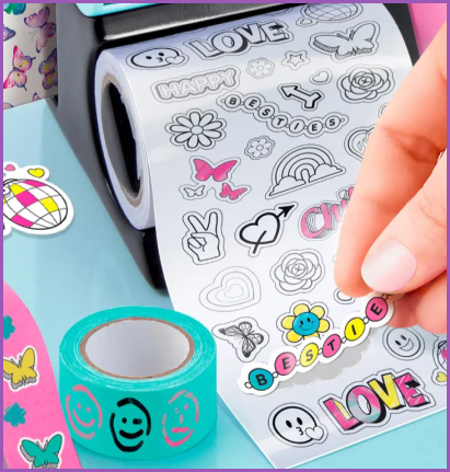 Użytkownik odkleja kolorową naklejkę z rolki Style 4 Ever Projekt Deko 3 w 1, przedstawiającą wzory takie jak serca, kwiaty, napisy i motywy przyjaźni, obok dekoracyjnej taśmy z uśmiechniętymi buźkami.