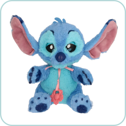 Pluszowa maskotka Psytulaski Stitch w odcieniach niebieskiego z dużymi różowymi uszami i różowym kwiatkiem na szyi, siedząca na jasnym tle.